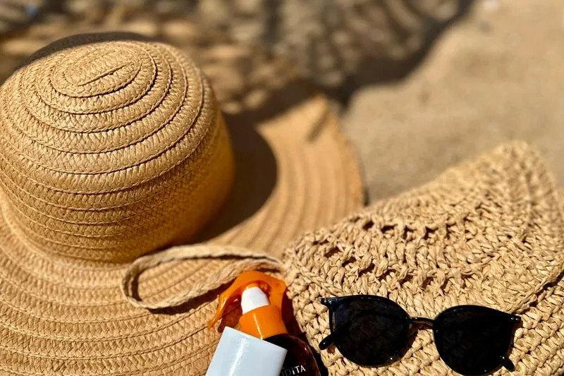 Straw hat, sunglasses and a bottle of sun cream laid out on the sand