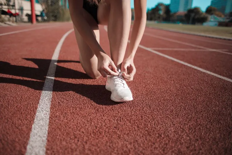 Woman kneeling on an athletics track, lacing up her white trainers