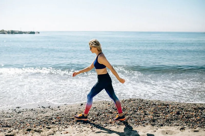 Woman in sports kit walking briskly along a pebble beach by the sea