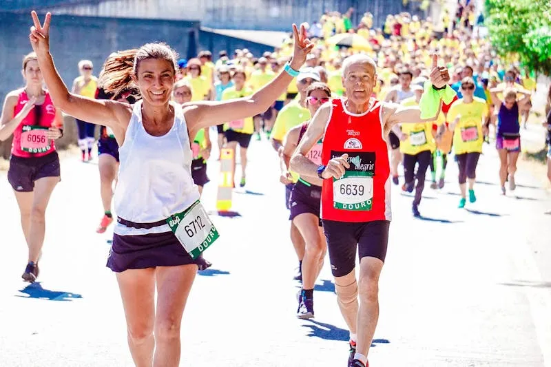 Runners wearing race numbers at a mass-participation road race, one woman smiling and making a victory sign