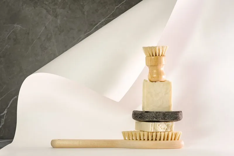 Stacked beige soap bars between a wooden dish brush and a long-handled natural-bristle brush