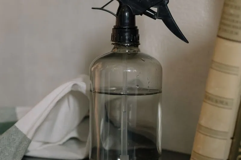Clear spray bottle filled with a clear liquid, next to a cotton tea towel and old books