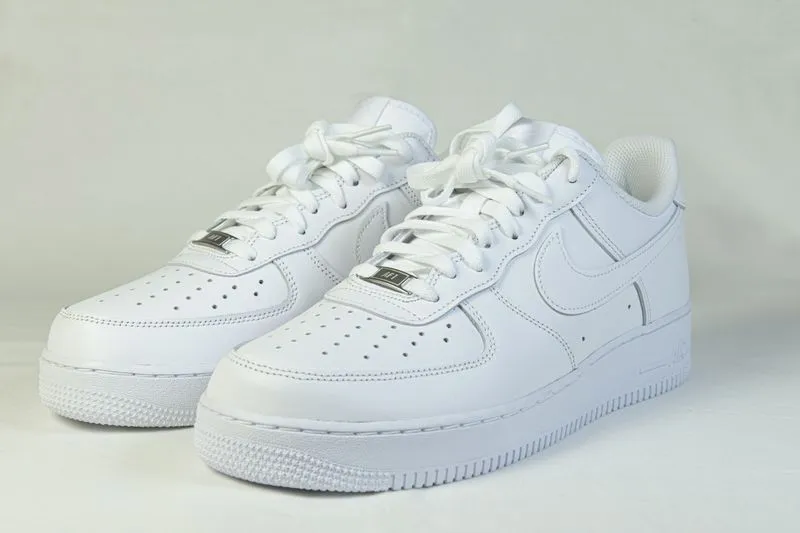 Pair of all-white low-top Nike Air Force 1 trainers against a light grey background