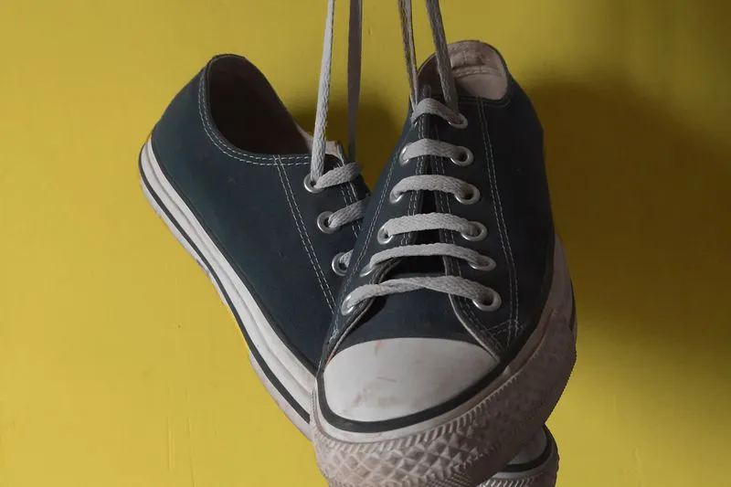 Pair of navy canvas low-top Converse hanging by their laces against a yellow wall