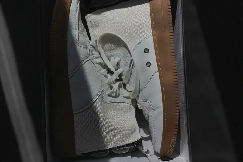 White leather high-top trainer with a gum sole, stored in its shoebox