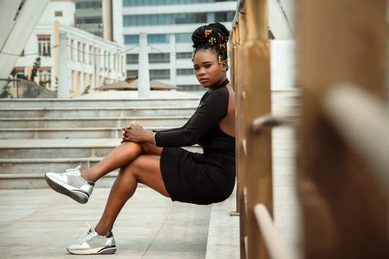 Woman sitting on a low city wall in a short, fitted black dress and silver trainers