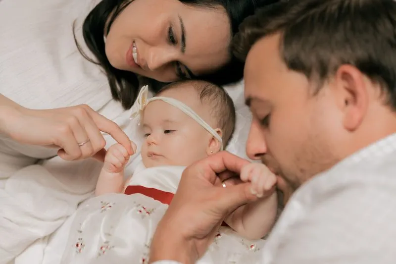 A mother and father lying either side of their baby, each absorbed in her