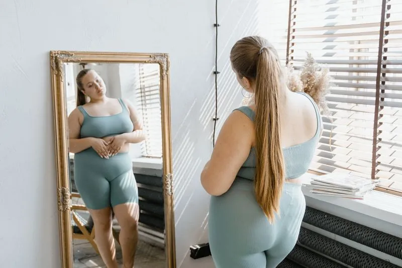 Woman in activewear looking at her stomach in a mirror