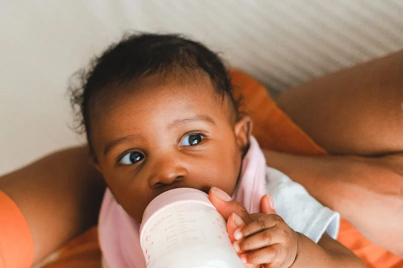Baby drinking from a bottle, held close by their mother