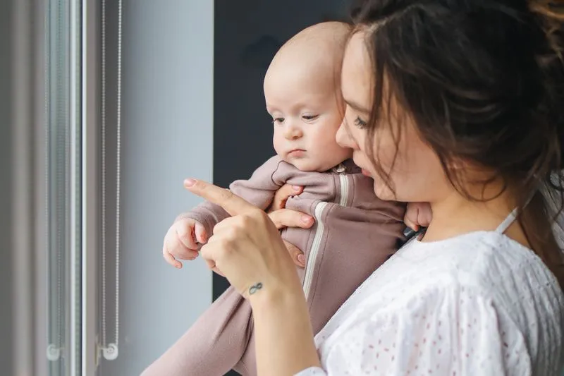 Young mother holding her baby close, pointing out the window together