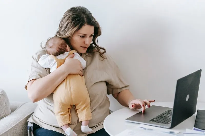 Mother working on her laptop with her baby against her shoulder
