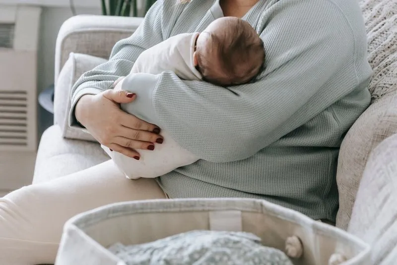 Mother sitting on a sofa, baby asleep nestled against her