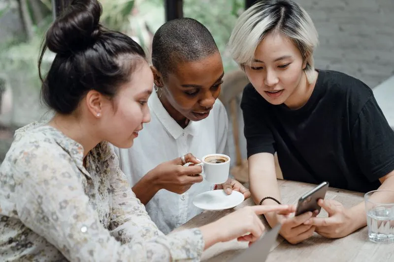 Three friends around a coffee, heads together over a phone