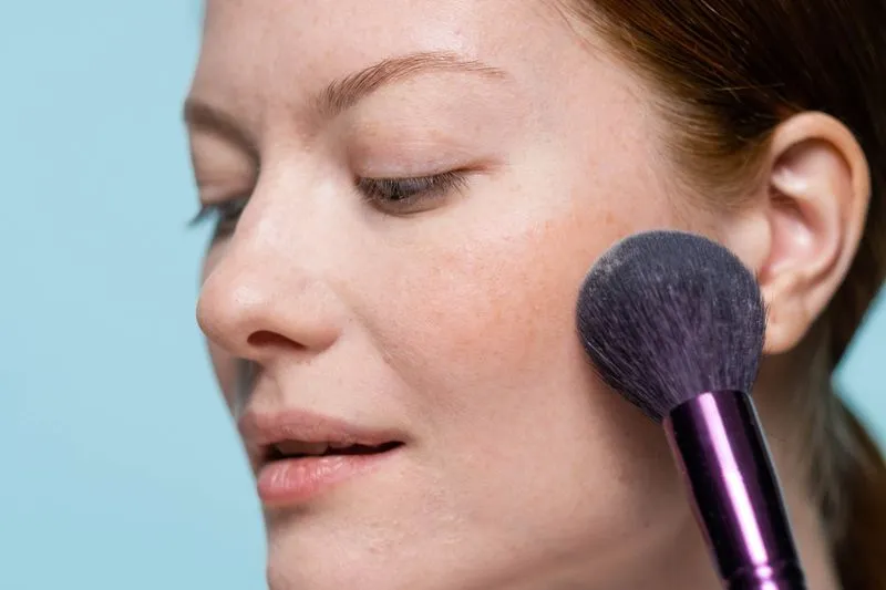 Blush brush sweeping across the cheekbone of a freckled woman