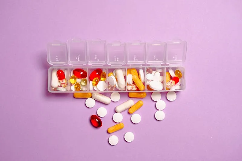 Open weekly pill organiser filled with colourful capsules and tablets on a lilac background