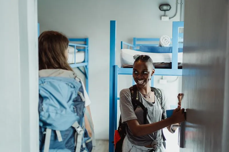 Two women with backpacks in a hostel dorm room with blue bunk beds
