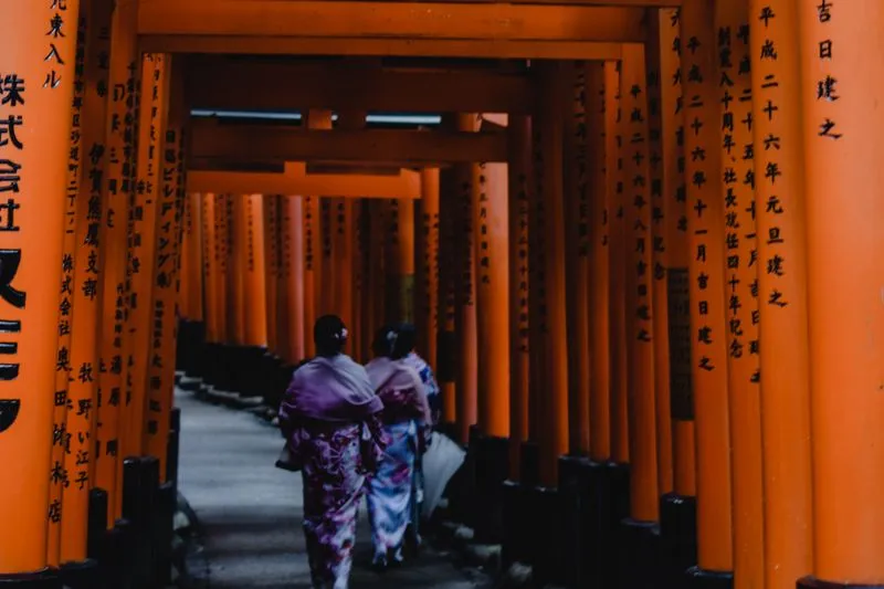 Two women in kimono walking through the orange torii gates of Fushimi Inari shrine in Kyoto