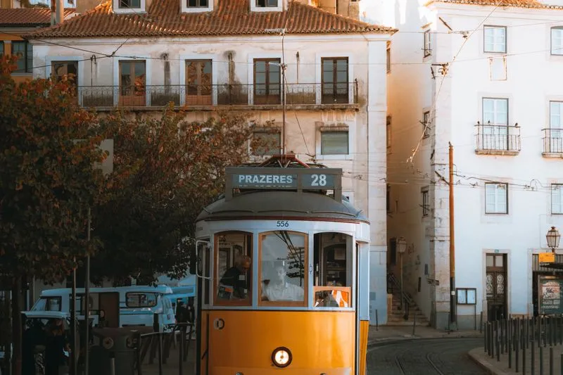 The yellow Tram 28 heading to Prazeres through a Lisbon street, evening light
