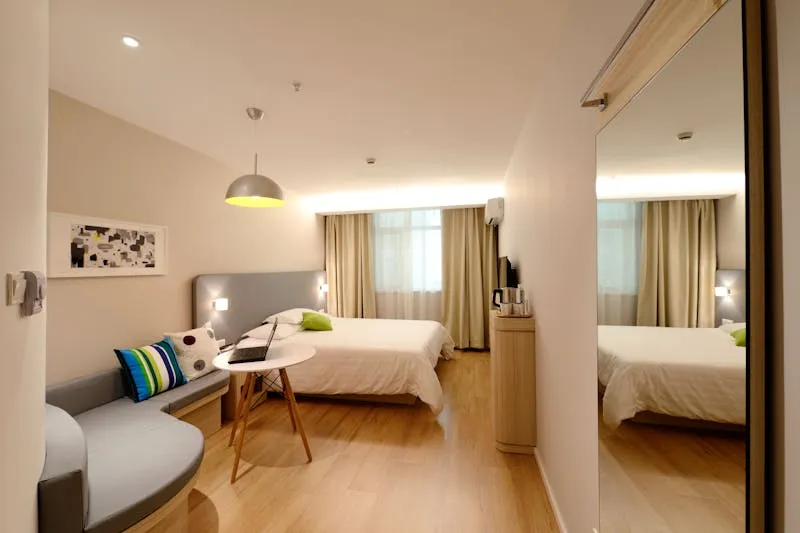 Modern hotel room in light tones, with a double bed, a sofa and a large mirror