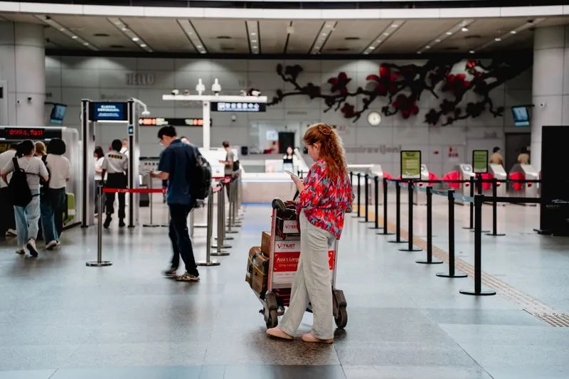 Traveller with a luggage trolley checking her phone in an airport hall