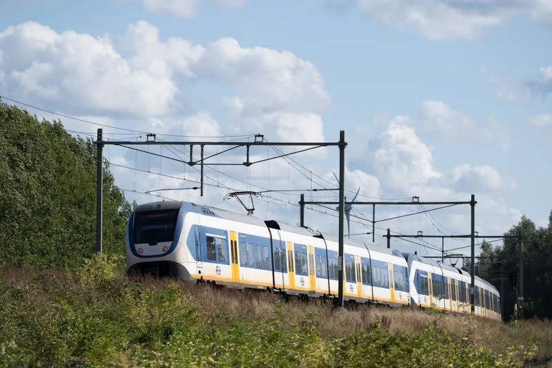 White, blue and yellow regional train running through open countryside under a cloudy sky