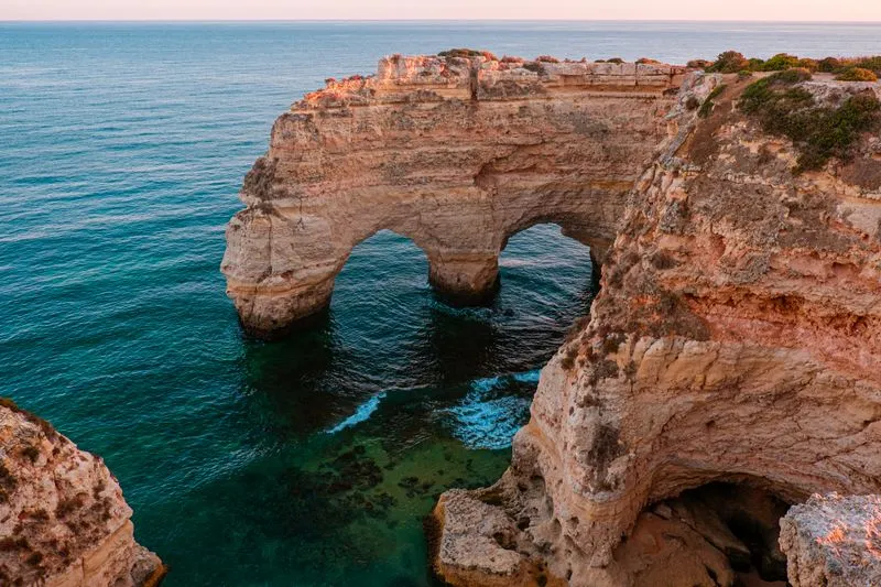 Natural double arch in the golden Algarve cliffs above a turquoise sea