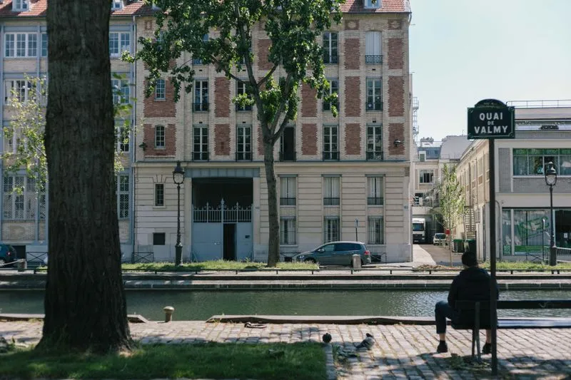Canal Saint-Martin seen from the cobbled quay: a Quai de Valmy street sign, trees and a brick-and-stone building on the far bank