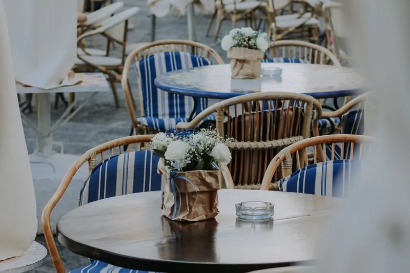 Café terrace with rattan armchairs, blue-and-white striped cushions and small bouquets on round tables