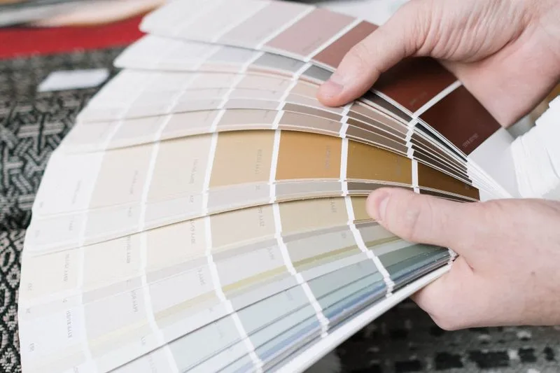 Hands fanning out a paint colour fan deck, from off-whites to browns and grey-greens