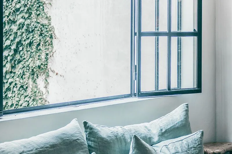 Window flung open above a bench with pale green linen cushions, white wall