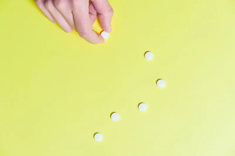 A hand picking up one white tablet from several on a yellow background
