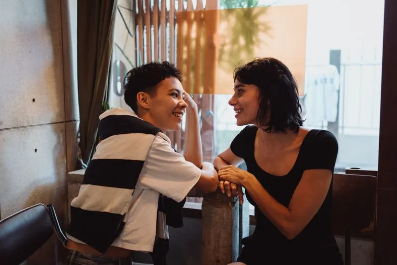 Two young women laughing and chatting, leaning on a cafe table