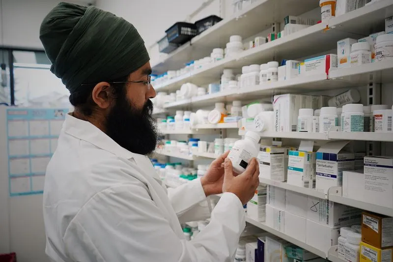 A pharmacist in a white coat checking a medicine bottle in front of pharmacy shelves