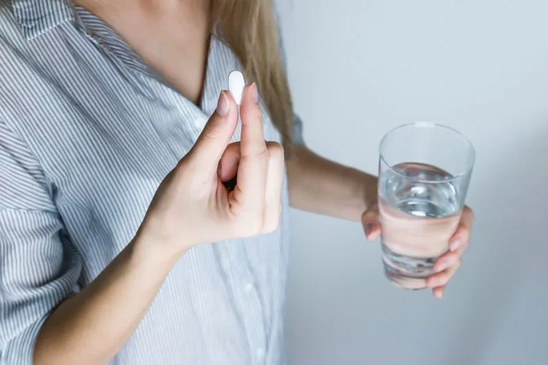 A young woman holding a white tablet between her fingers and a glass of water in her other hand
