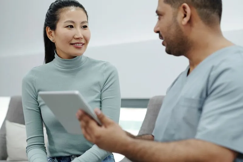 A young woman in a consultation with a healthcare professional in scrubs holding a tablet