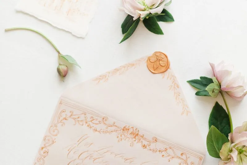 Cream envelope addressed in orange calligraphy ink, closed with a wax seal, among hellebores