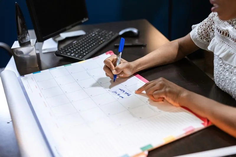 A hand writing a date in blue pen on a large monthly desk calendar