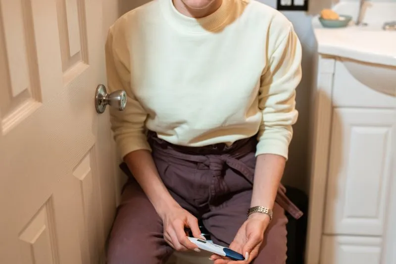 A woman sitting in a bathroom holding a digital pregnancy test in her hands