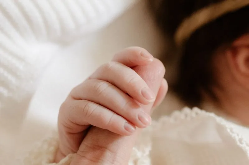 Close-up of a newborn's hand gripping an adult's finger, in soft light