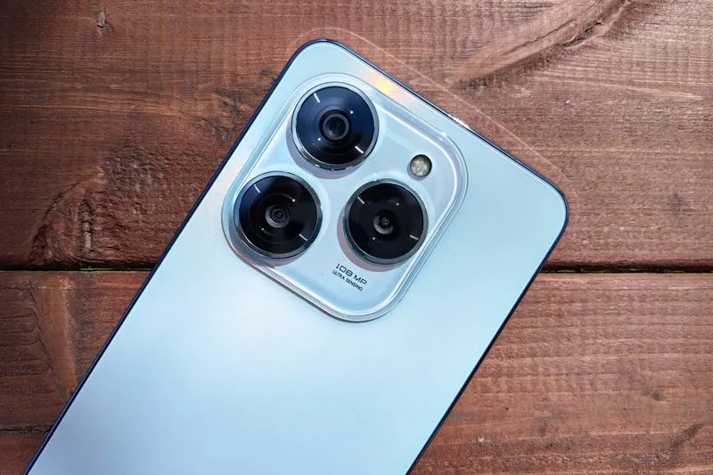 Pale blue smartphone lying face down on a wooden table, its camera lenses facing up