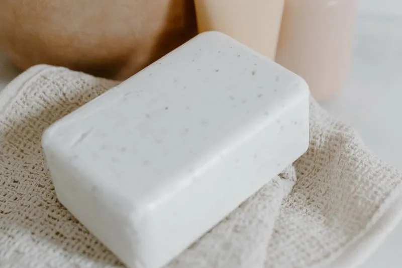 White bar of soap on a waffle-weave cotton towel, with two pale bottles behind it