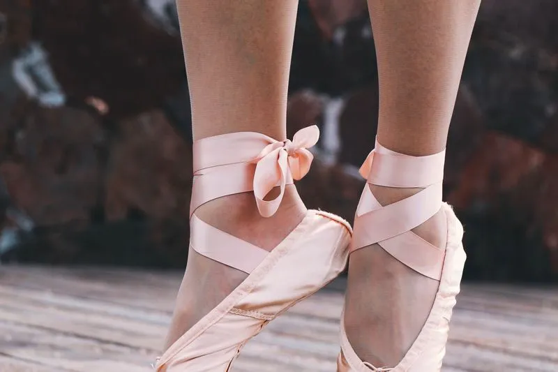 Close-up of pale pink ballet shoes with satin ribbons crossed and tied around the ankles
