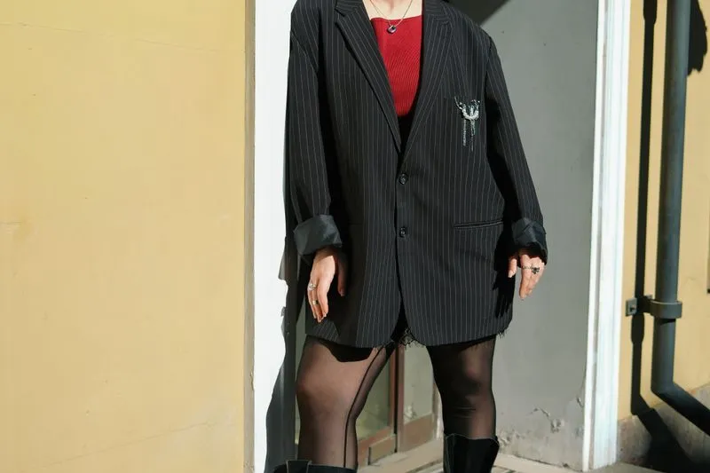 Oversized black pinstripe blazer with rolled-up sleeves, worn over a red top with sheer black tights and boots