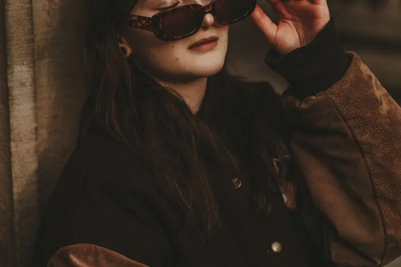 Woman in tortoiseshell sunglasses wearing a chocolate-brown jacket with suede sleeves