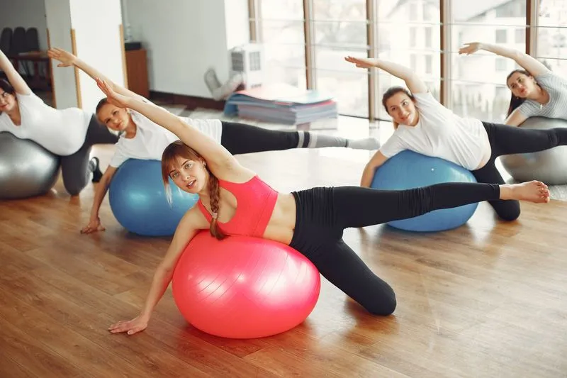 Women in an exercise class leaning sideways over large exercise balls, one arm stretched overhead