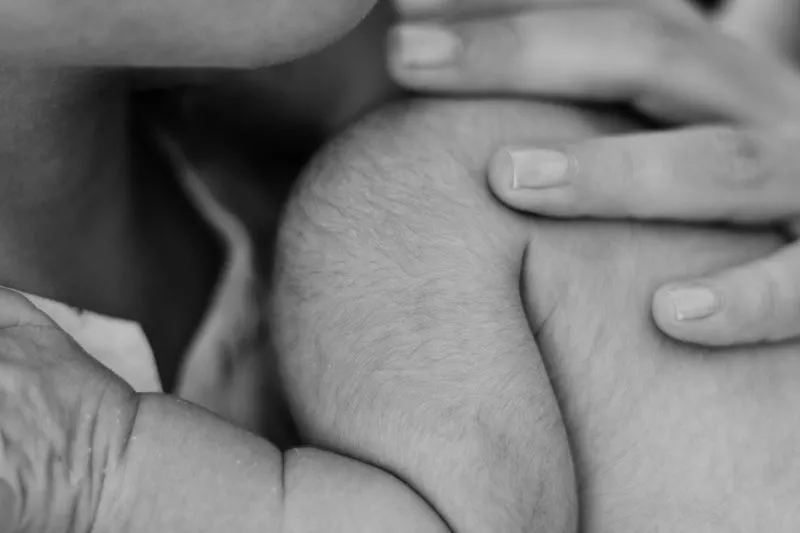 Black-and-white close-up of a newborn nestled skin to skin against its mother's chest, held by her hand
