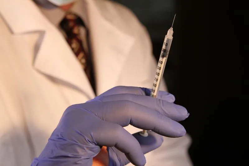 Gloved hand of a doctor in a white coat holding a fine syringe, needle pointing up