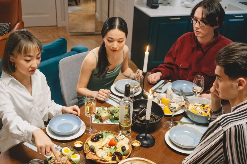 Group of young friends around a candlelit table, sharing several dishes and glasses of white wine