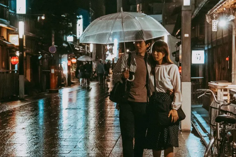Couple huddled under a clear umbrella in a wet cobbled lane at night