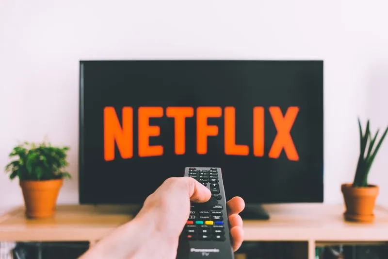 Hand pointing a remote at a TV showing the Netflix logo
